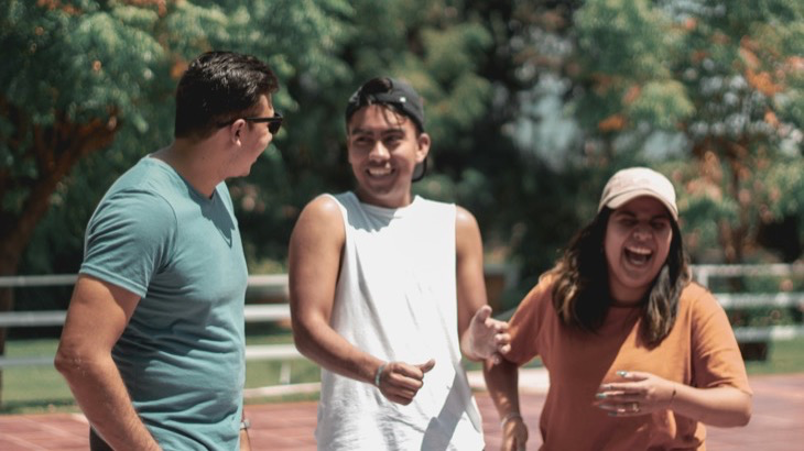 Three friends laughing together outdoors on a sunny path, an example of a recurring social habit built around a standing weekly meetup