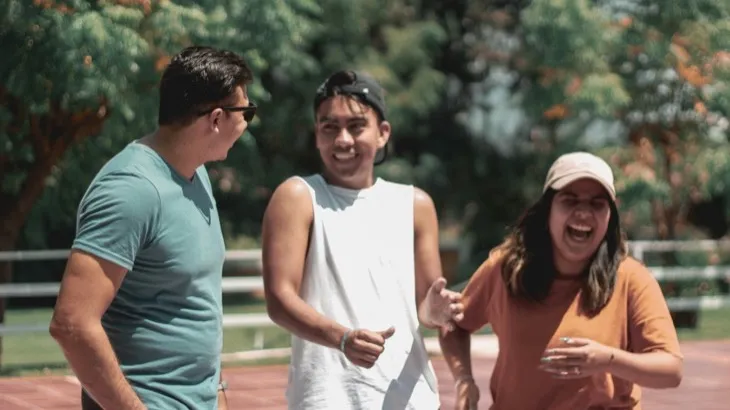 Three friends laughing together outdoors on a sunny path, an example of a recurring social habit built around a standing weekly meetup