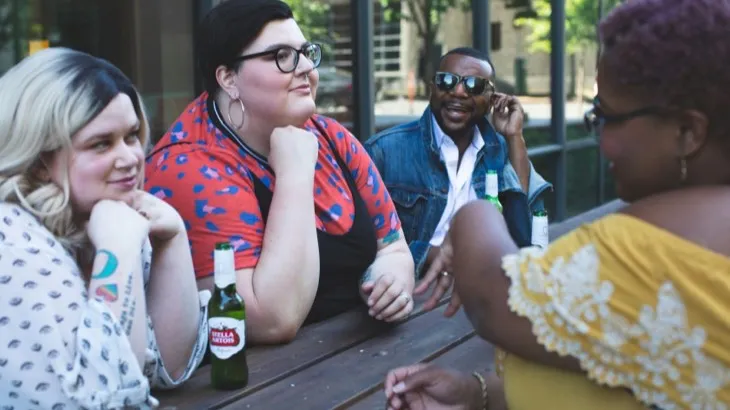 Four friends talking around an outdoor table at a local bar, the kind of regulars a business community chat app turns into a group