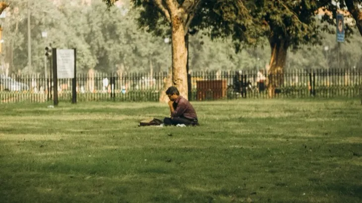 Person sitting peacefully reading a book in a park, representing digital wellness and mindful technology use