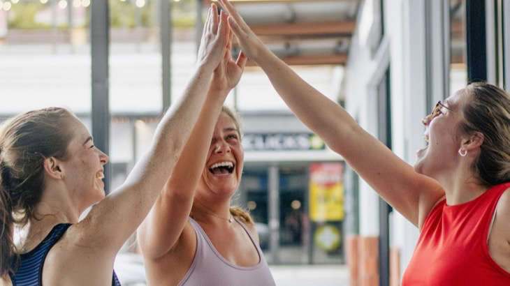 Three friends high-fiving after a workout, celebrating a shared healthy habit streak