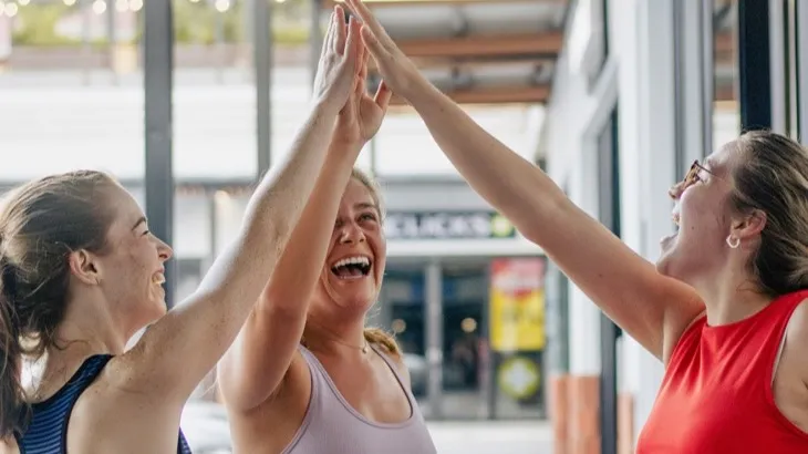 Three friends high-fiving after a workout, celebrating a shared healthy habit streak