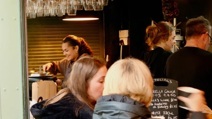 Regular customers talking at the counter of a busy neighborhood cafe, the audience a small business loyalty program is built for