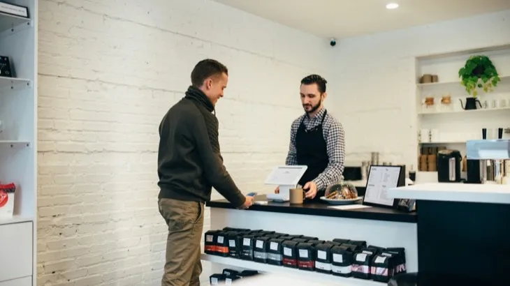 A customer paying at the counter of a small independent coffee shop, the moment a loyalty program is won or lost