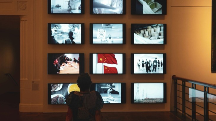 Person standing before a wall of television screens displaying various media, representing information overload and the need for media literacy