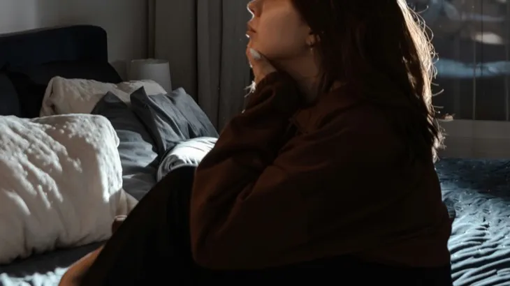 Young person sitting on a bed at night in dim light, the scenario the settlement's overnight lockout targets